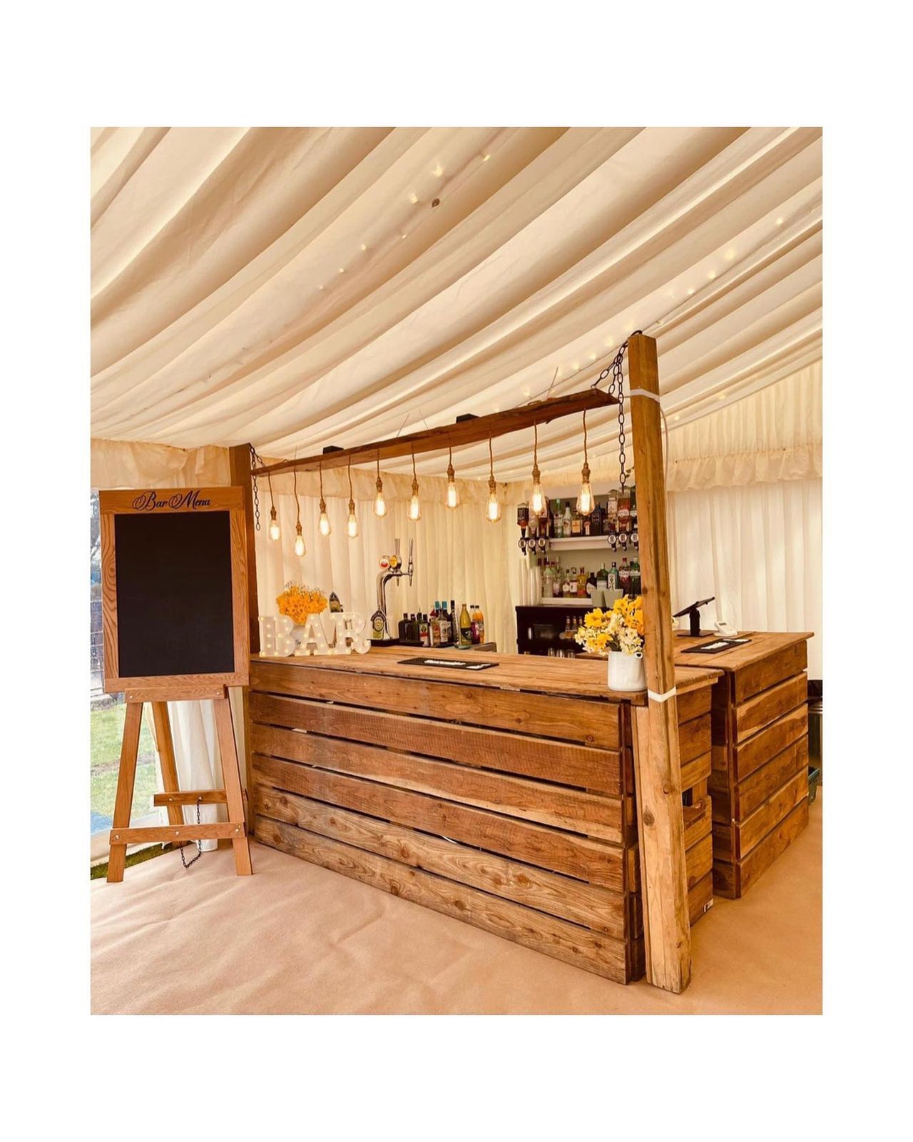 Plank bar with hanging festoon filament bulbs in a lined marquee